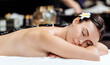 © wedmoments.stock - Female client receiving hot stone therapy in a spa, black stones on her back, white towel, tropical flower in hair, relaxing in a serene environment. Concept spa, hot stone massage, relaxation, wellne