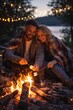 © Juan - Couple sitting by campfire wrapped in blanket during night by lakeside enjoying warmth together
