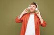 © ViDi Studio - Young smiling stylish happy fun student man he wear basic white t-shirt orange shirt listen enjoy music in headphones isolated on plain pastel green wall background studio portrait. Lifestyle concept