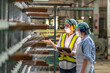 © BESTIMAGE - Textile inspection factory teamwork female supervisor in safety vest checking and discussing yarn production quality with woman worker in textile mill holding thread spool and clipboard.