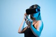 © Volodymyr_sh - Woman using virtual reality headset and interacting with digital interface using hand gesture in modern blue studio lighting