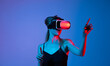 © Volodymyr_sh - Woman experiencing virtual reality with hand gestures under neon blue and red lighting, immersive VR technology and futuristic digital concept