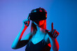 © Volodymyr_sh - Young woman playing VR game using virtual reality headset and hand gestures in futuristic neon light studio environment