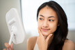 © Chanakon - Beautiful asian woman touching her smooth glowing skin with closed eyes, smiling in mirror reflection. Confident girl proud of natural beauty and healthy skincare results.
