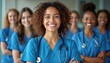 © miss irine - Diverse team of nurses stands together smiling confidently. Medical professionals wear blue scrubs and stethoscopes. They represent healthcare team unity and compassionate patient care.