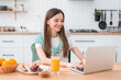 © InsideCreativeHouse - Young woman working remotely at home kitchen table with laptop healthy breakfast, representing freelance lifestyle, flexible schedule, and modern work-from-home concept.