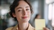 © CYBERPINK - Close-up portrait of a young woman holding a yellow sticky note in her hand. she is looking up at the camera with a slight smile on her face.