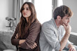 © luciano - Young couple sitting back to back on couch having a dispute, expressing relationship conflict, unresolved problem or question, emotional distance, or communication problems in a modern living room.