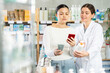 © JackF - Selective middle-aged woman scanning QR on cream while female pharmacist giving offer in chemistry