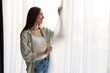 © New Africa - Happy woman near window with beautiful curtains at home