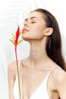 © VICHIZH - Graceful model with long hair holding a vibrant flower, exuding serenity and beauty in a minimalistic white backdrop.
