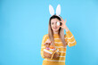 © New Africa - Easter celebration. Smiling woman in headband with bunny ears and wicker basket full of painted eggs on light blue background, space for text
