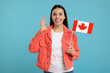 © New Africa - Happy woman with flag of Canada showing Ok on light blue background