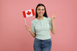 © New Africa - Happy woman with flag of Canada showing peace gesture on pink background