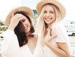 © halayalex - Two young beautiful smiling hipster female in trendy summer white dress clothes and straw hats. Sexy carefree women walking in street. Positive models having fun, hugging and laughing