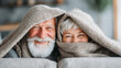© Umaporn - A smiling older couple cuddled on a couch under a blanket, capturing cozy living, winter comfort, and a relaxed retirement lifestyle.