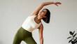 © Anna - A fit woman in activewear practicing a yoga side bend stretch. Young Indian person doing a flexibility workout indoors against a plain background. Healthy lifestyle and wellness concept
