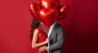 © NeuroCake - Couple kissing behind red heart balloons on red background. Romantic man and woman embracing for Valentine's Day celebration