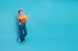 © deagreez - Young stylish woman in casual chic outfit points to the right against a bright blue background