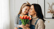 © narumiaegis - Heartwarming scene a happy mother embracing her joyful daughter, who presents vibrant spring tulips, symbolizing their beautiful family bond and shared happiness