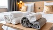 © lililia - White and gray towels are stacked on a wooden surface in a hotel room with beds and decorative pillows in the background