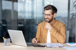 © Liubomir - Young businessman happily engaging with his computer, focused on work and innovation at a modern office desk, embodying success and digital communication