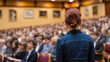 © Macrostock - Medium shot of a speaker addressing a lively crowd in a community hall encouraging public involvement in social initiatives.