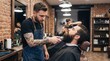 © Saqib GFX - Professional male barber with tattoos and apron trimming beard of client in modern barbershop. Hairdresser using electric clippers. Men grooming concept. Stylish haircut salon