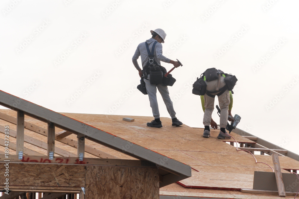 Workers installing OSB roof sheathing on two-story wooden home under ...