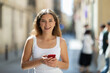 © JackF - Young woman looking to phone in hands and chatting in city