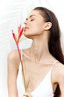 © VICHIZH - Elegant model with long hair gently holding a tropical flower, showcasing a serene expression against a soft, bright background.