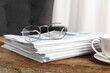 © Pixel-Shot - Stack of newspapers with cup of tea and eyeglasses on wooden table in office