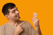 © Pixel-Shot - Young man pointing at blisters of vitamin A pills on yellow background, closeup