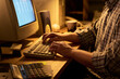 © pressmaster - Middle aged Caucasian man working on desktop computer in dimly lit office, typing on keyboard with both hands, calculator and coffee mug visible on wooden desk