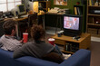 © pressmaster - Caucasian man and woman sitting on couch watching television together holding drinks, vintage electronics and retro decor visible in background