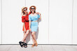 © halayalex - Two young beautiful smiling hipster women in trendy summer same clothes. Carefree models posing in the street. Positive models having fun. Cheerful and happy. In hat and sunglasses. Near wall
