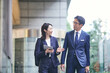 © amanaimages - 会話をしながら屋外を歩くビジネスマンとビジネスウーマン