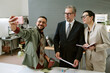 © AnnaStills - Young adult man taking selfie with middle aged man and young adult woman standing together in modern office holding documents and notebook