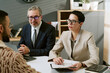 © AnnaStills - Caucasian middle aged man and Caucasian middle aged woman interviewing young adult man in modern office setting, both interviewers wearing glasses and holding documents