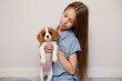 © GRON777 - Young girl in denim dress holds spaniel puppy in arms against neutral wall in room. Meeting new pet, touching adoption scene. Concept pet care and human-dog friendship.