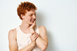 © SHOTPRIME STUDIO - Young man with red hair wearing white tank top laughing and touching face on white background. Casual style, happy expression and natural smile with playful mood in studio.
