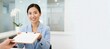 © Fernando - Asian woman, receptionist, handing clipboard with document to client at modern office reception desk, smiling warmly, professional service, welcoming atmosphere, business interaction, customer service