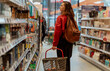 © olezzo - Young woman with shopping basket choosing cosmetics and household products in store aisle