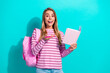 © deagreez - Young woman student with pink backpack and notebook smiling excitedly against teal background showcasing study fashion and cheerful lifestyle