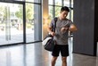 © Meow Creations - Young Asian man checks fitness tracker while walking to gym