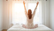 © Guillotine - Woman stretching with arms raised on bed in bright bedroom morning
