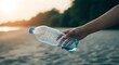 © MD - Hand holding a plastic water bottle on a beach at sunset