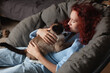 © Tatyana Gladskih - Beautiful redhead Woman sitting on sofa laughing and cuddling Cat indoor at home