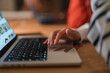 © Studio Marmellata - A person's hand is shown using a laptop's touchpad, with the screen displaying images. The scene is set on a wooden desk.