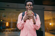 © BullRun - Urban African freelancer smiling at camera while holding phone, presenting approachable confidence and tech immersion in a mobile-focused freelance career.